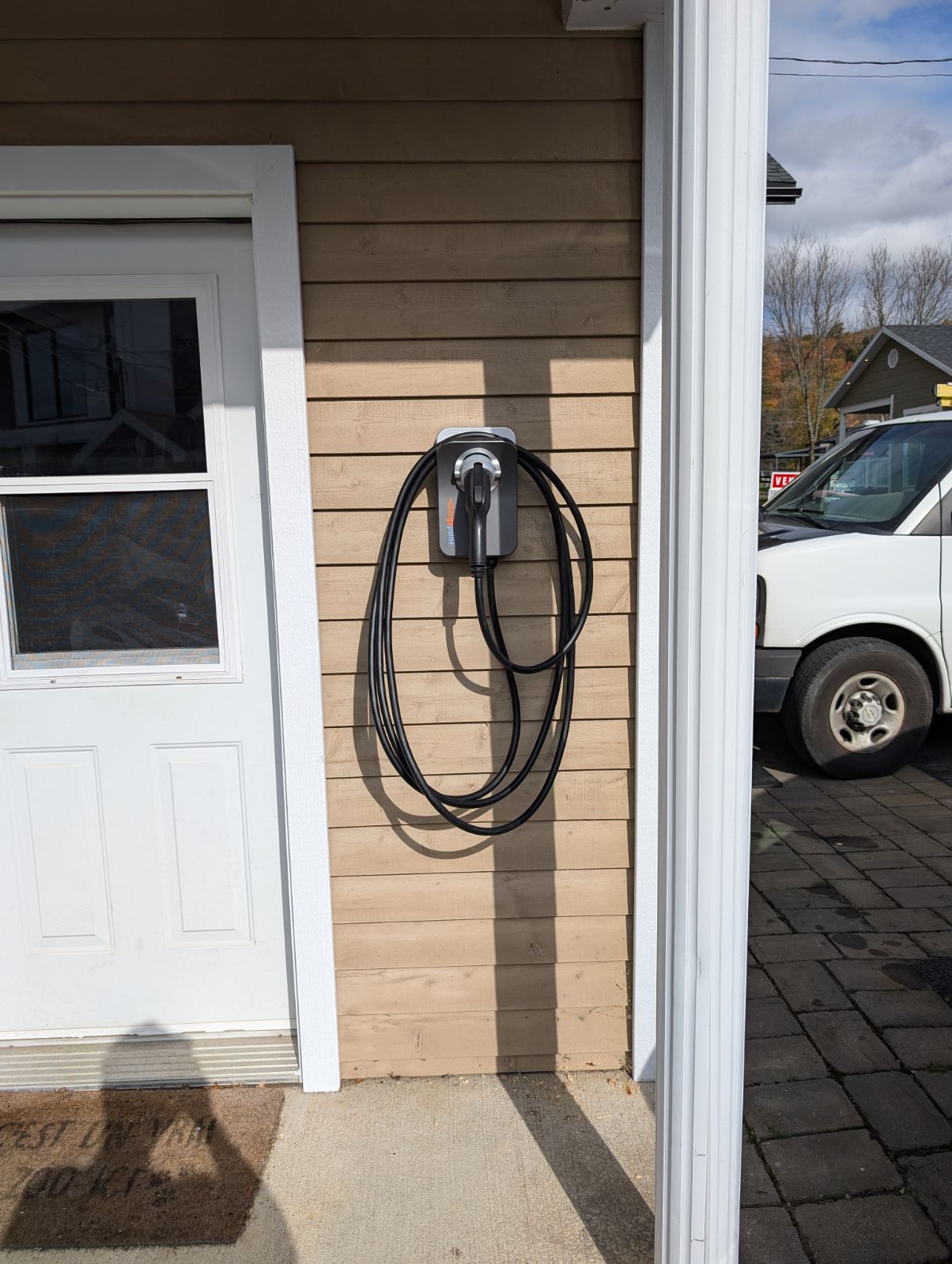 Borne de recharge pour voiture électrique installée sur le mur extérieur d’un garage résidentiel, avec câble enroulé proprement.