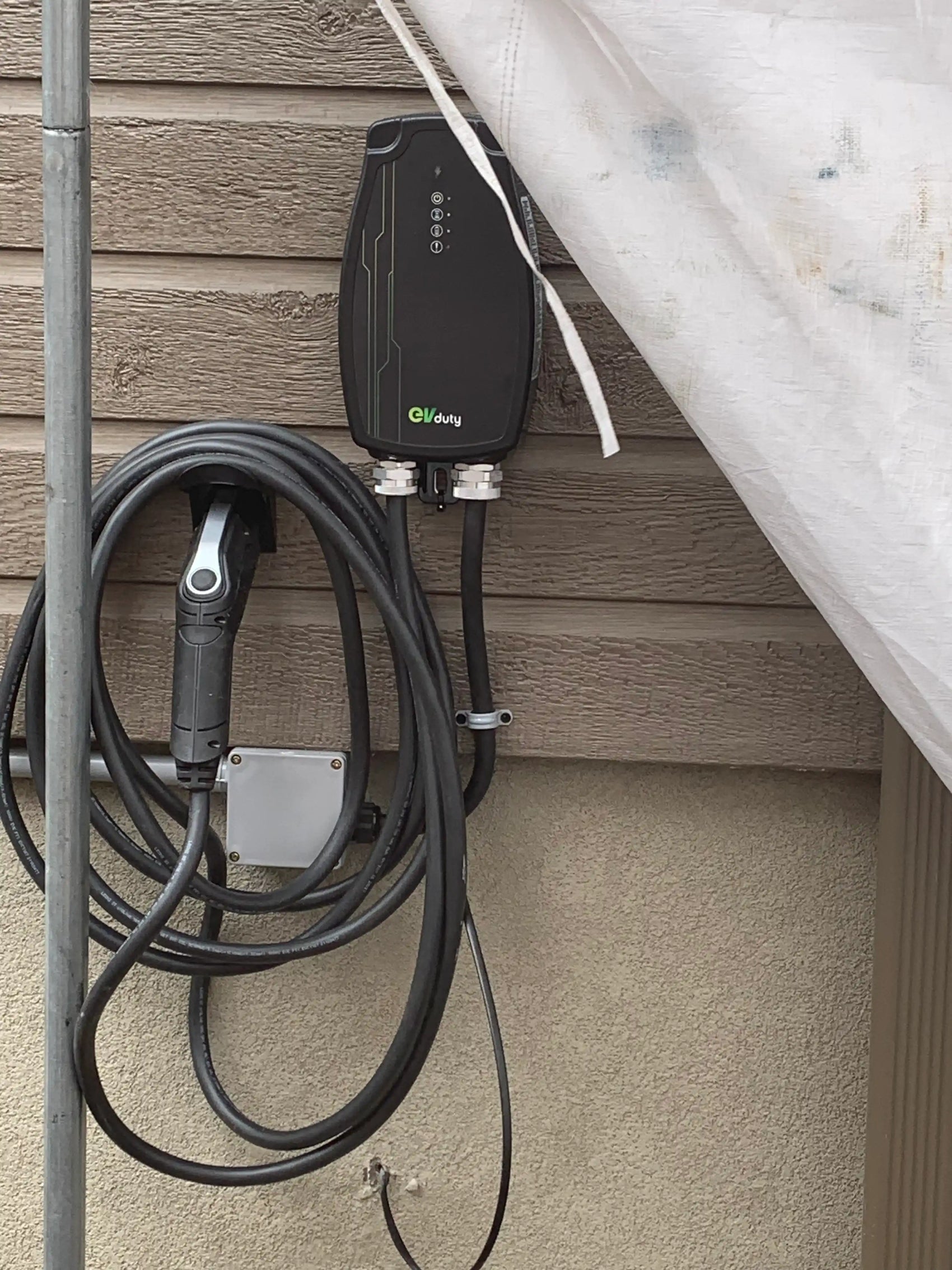 Borne de recharge EVduty fixée à un mur extérieur, avec câble et connecteur pour véhicule électrique soigneusement enroulés autour du support.